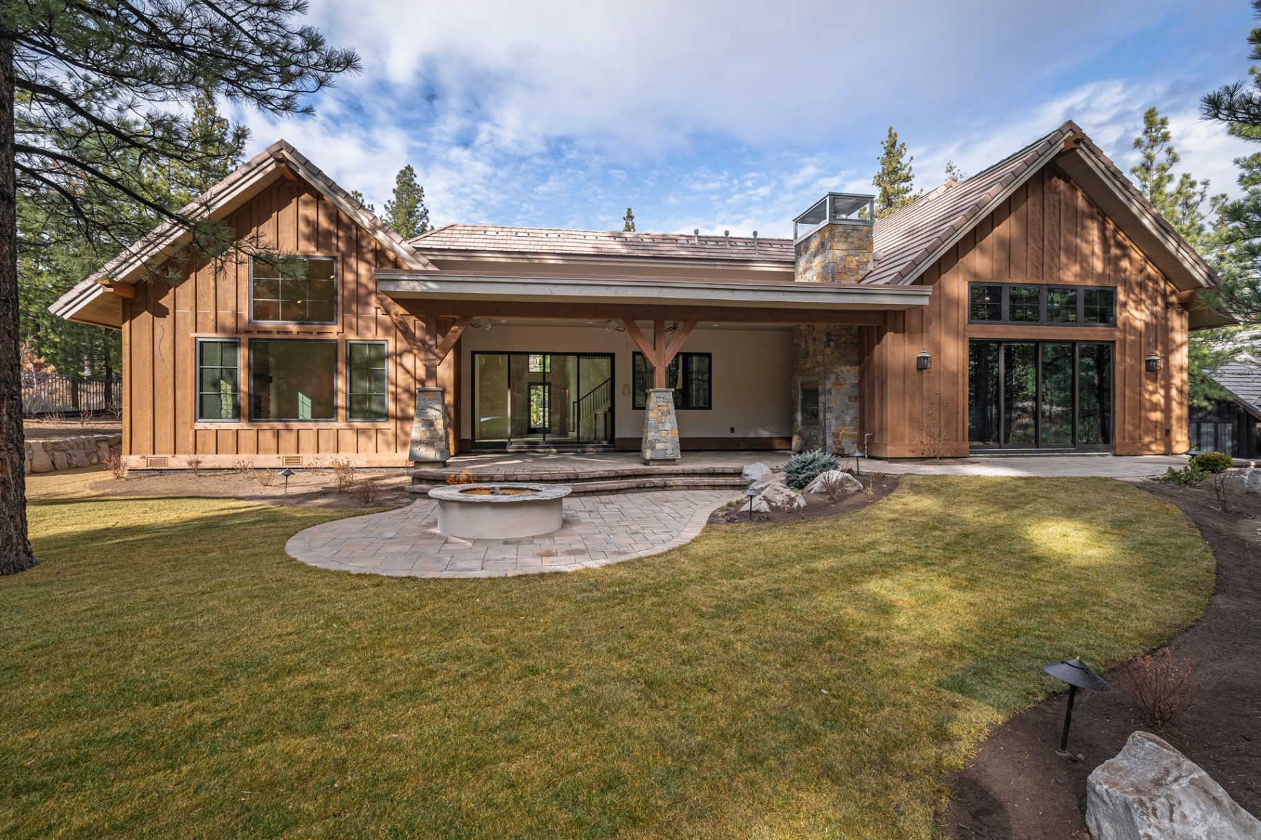 Rear exterior with board-and-batten cedar, stone chimney, and covered loggia