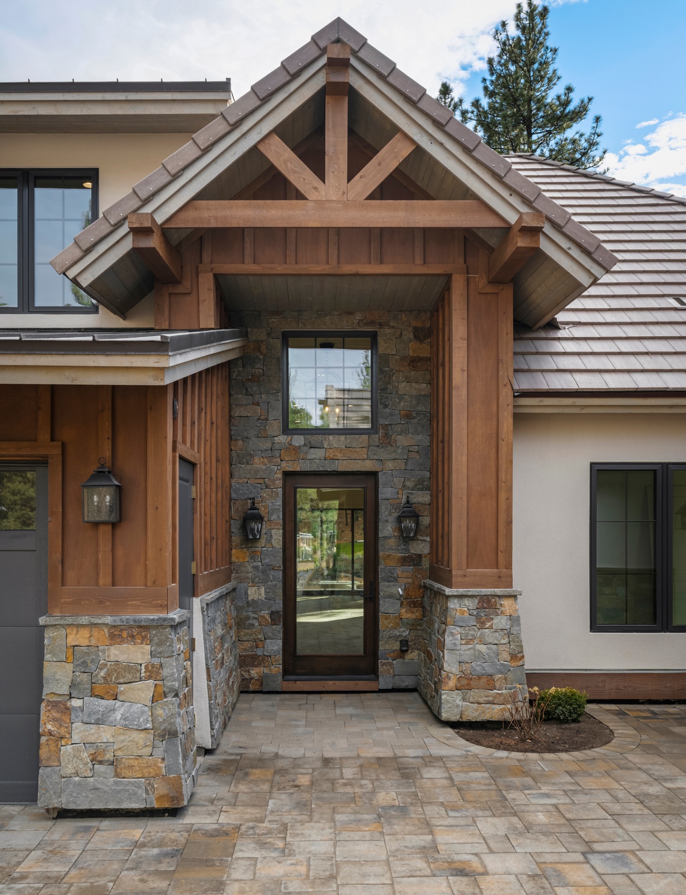 Timber-framed portico entry with dry-stack stone columns and iron lanterns