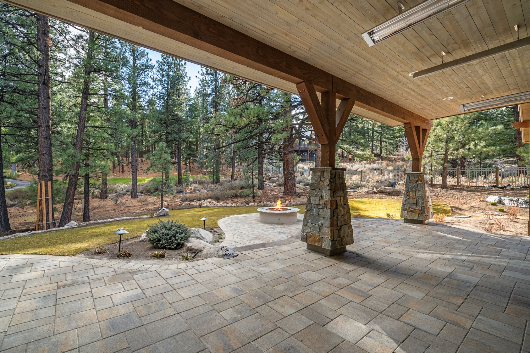 Covered patio with timber beams, radiant heaters, and stone fire pit