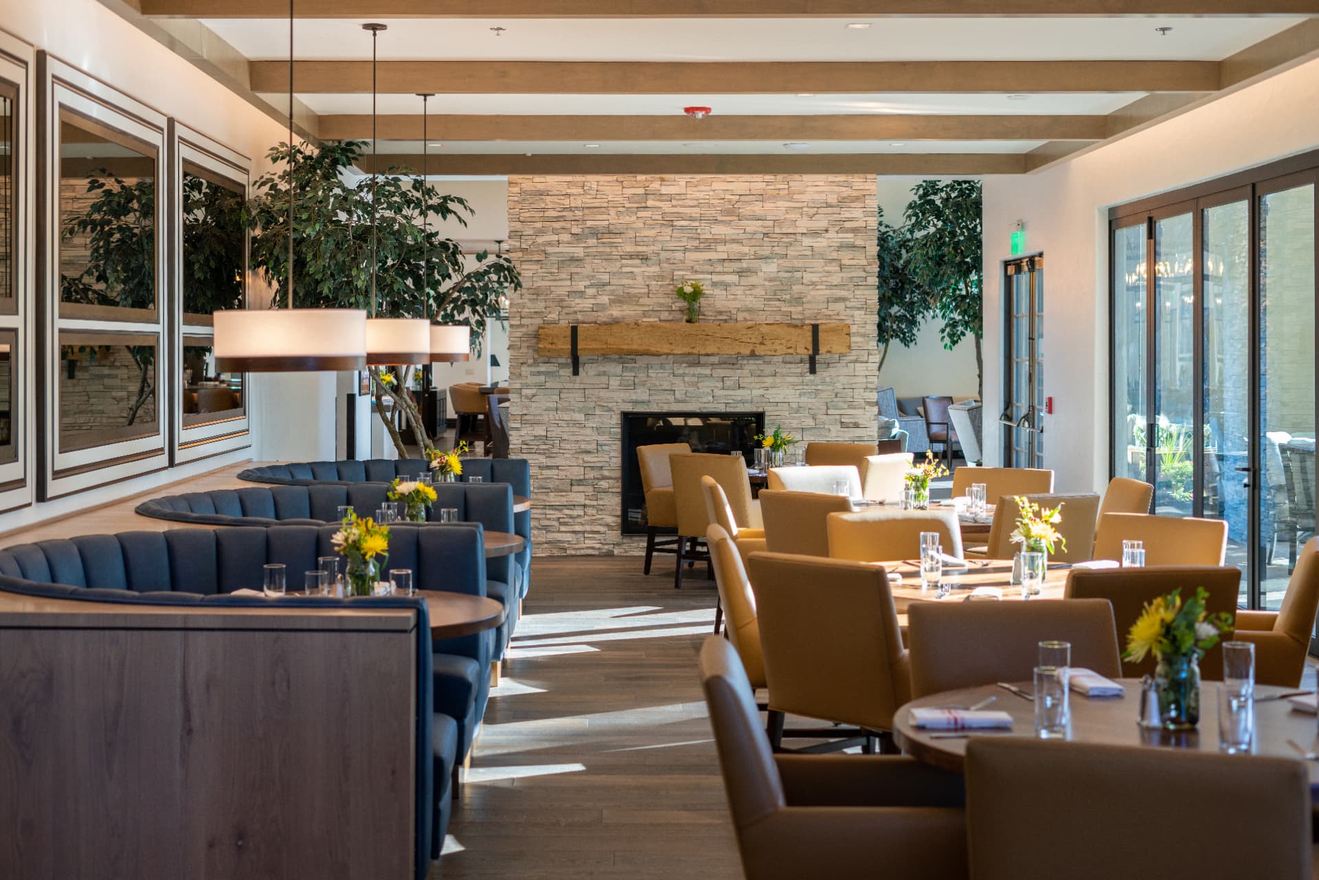 Montreux clubhouse dining room with stacked-stone fireplace, reclaimed timber mantel, and curved banquette seating